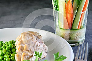 Fried chicken breast with broiled green peas and a glass with thin slices of carrot and cucumber closeup. Healthy food concept