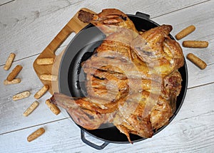 Fried chicken. On the table in a cast-iron pan, with a crisp, Golden crust. Bread sticks with sesame seeds. Wooden background