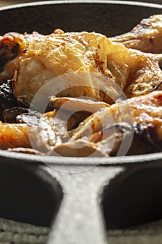 Fried chicken drumsticks and sliced mushroom n a cast iron frying pan. On a wooden chopping board