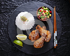 Fried chicken legs with teriyaki sauce sesame seeds and rice on black stone