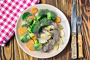 Fried chicken liver with vegetables apples broccoli carrots onions and herbs on a dish on the wooden table, horizontal view from a