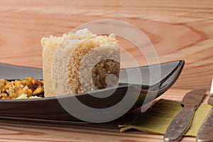 Fried chicken meat and couscous on black plate on wooden table