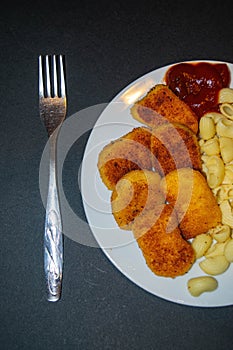 Fried chicken nuggets and boiled pasta with ketchup on a white plate on a dark background. Close up