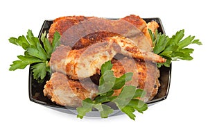 Fried chicken pieces coated with breadcrumbs with with parsley on a black plate. Isolated on white background