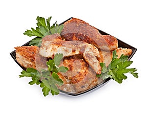 Fried chicken pieces coated with breadcrumbs with with parsley on a black plate. Isolated on white background