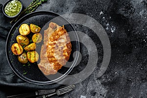 Fried Chicken schnitzel with baked potatoes. Black background. Top view. Copy space