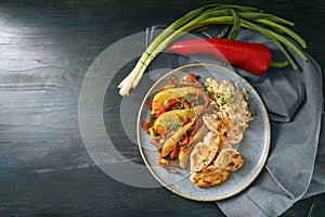 Fried chicken slices with brown whole grain rice and vegetables like bell pepper, leek and pear on a blue plate and a dark wooden