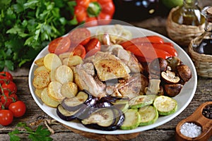 Fried chicken slices with potatoes,  bell peppers, eggplant, zucchini, cherry tomatoes, mushrooms and onions on a wooden backgroun