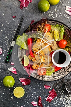 Fried chicken with soy sauce and vegetables on a black plate, view from the top