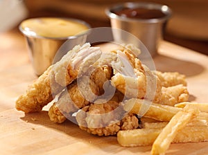 Fried chicken strips with french fries and sauce.