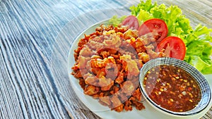 Fried chicken tendon served with sweet chilli sauce and green salad on white plate.