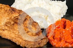 Fried chicken white meat with mashed potatoes and paprika ajvar on the black plate