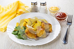 Fried chicken winglets in breading with potato in plate, bowls with sauces, pepper, salt, fork