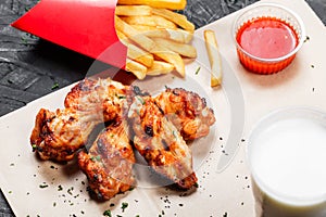 Fried chicken wings with baked potatoes and bbq sauce on craft paper on black background.