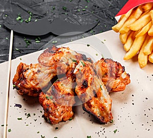 Fried chicken wings with baked potatoes and bbq sauce on craft paper on black background.