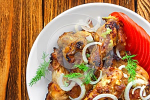 Fried chicken wings close-up, with fresh tomatoes, onions, dill, garlic on a wooden background. View from above.