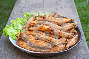 Fried chicken wings with fish sauce with salad vegetables on a white plate placed on a wooden table.