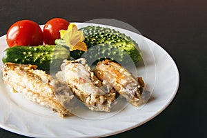 Fried chicken wings with fresh cucumber and tomatoes on a white plate on a black background. Copy space