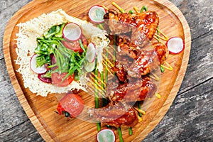 Fried chicken wings with fresh salad, grilled vegetables and bbq sauce on cutting board on wooden background