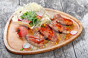 Fried chicken wings with fresh salad, grilled vegetables and bbq sauce on cutting board on wooden background