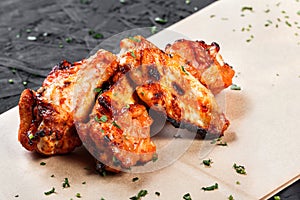 Fried chicken wings with greens on craft paper on black background.