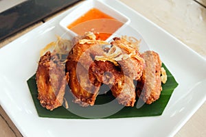 Fried chicken wings with sauce in white plate on wooden table.