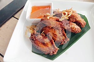 Fried chicken wings with sauce in white plate on wooden table.