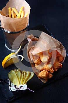 Fried chicken wings on the table. Crispy fried chicken in batter. French fries in paper. Slices of pickled cucumber