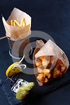 Fried chicken wings on the table. Slices of pickled cucumber. Crispy fried chicken in batter. French fries in paper