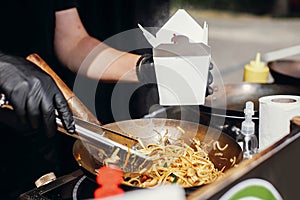 Fried chinese japanese noodles with vegetables and shrimps in takeaway box.Food delivery. Chef putting noodles in carton box to go