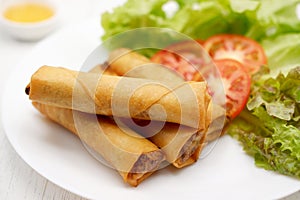 Fried Chinese spring rolls in a white plate, on white wooden table.