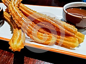 Fried Cinnamon Churros with dark chocolate dipping sauce served on white plate