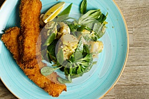 Fried cod fish fillet with potato salad, dijon mustard and a slice of lemon on a plate