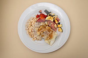 fried cod fish with onion, vegetables, rice and olive oil on plate