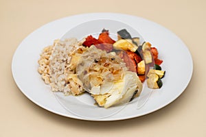 fried cod fish with onion, vegetables, rice and olive oil on plate