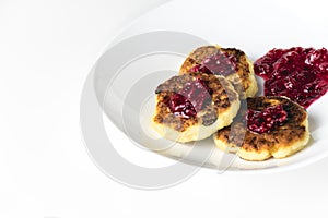 Fried cottage cheese pancakes on a white plate. Syrniki with red jam on top