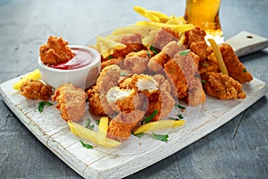 Fried crispy chicken nuggets with french fries, ketchup and beer on white board