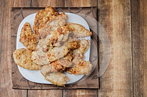 Fried crispy nuggets in a white bowl on a wooden table. Top view, copyspace. Chicken strips