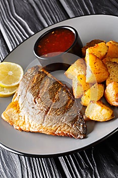 Fried dorado fillet with potatoes and sauces close-up on a plate. vertical