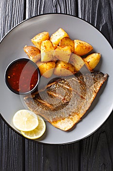 Fried dorado fillet with potatoes and sauces close-up on a plate. Vertical top view