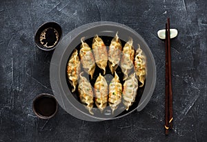 Fried dumplings Gyoza in pan, soy sauce, chopsticks on dark stone background