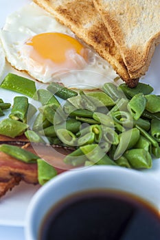 Fried egg, bacon, green beans, toastsand white cup of coffee on light background. English breakfast.