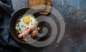 Fried egg, bacon and sausages in a skillet on dark stone background