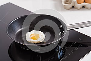 Fried egg in black pan during cooking on induction electric cooktop