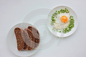 Fried egg with green peas on a white plate and rye bread on white table background. Healthy breakfast or brunch concept. Sunny sid