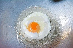 A fried egg with oil on pan.