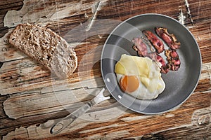 Fried Egg and Pork Ham Rashers In Teflon Frying Pan With Slice Of Brown Bread Set On Old Cracked Wooden Picnic Table photo