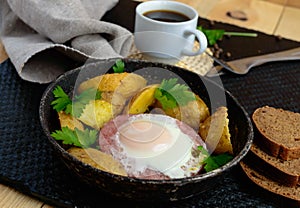 Fried egg in salami and baked potatoes. Submission of a frying pan with a cup of coffee and rye bread