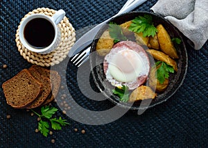 Fried egg in salami and baked potatoes. Submission of a frying pan with a cup of coffee and rye bread