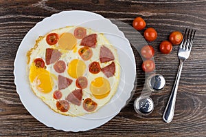 Fried egg with sausage and tomatoes in dish, salt, pepper